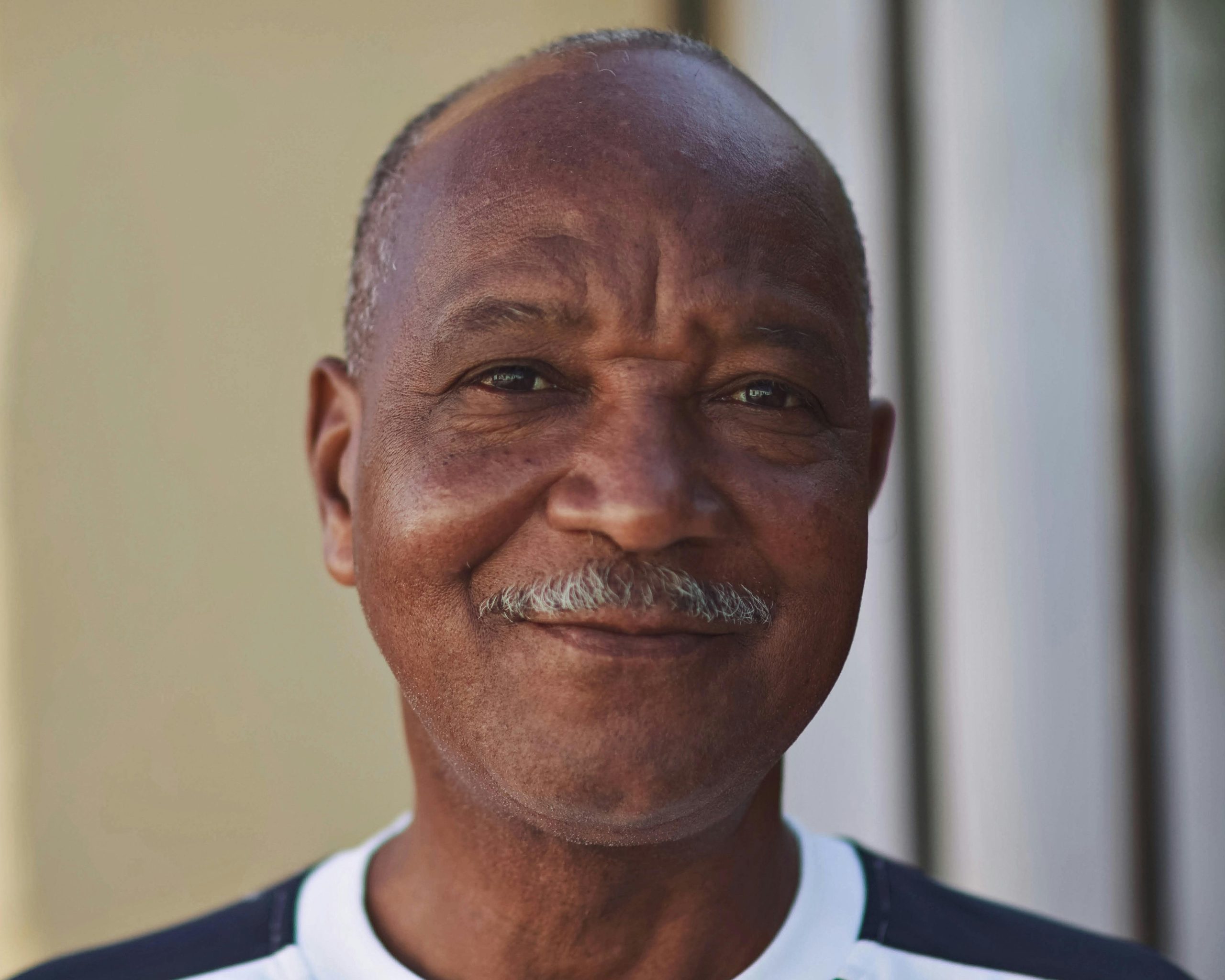 A joyful portrait of an elderly African man with a mustache, enjoying the sunlight.